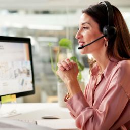 woman with headset looking at two computers