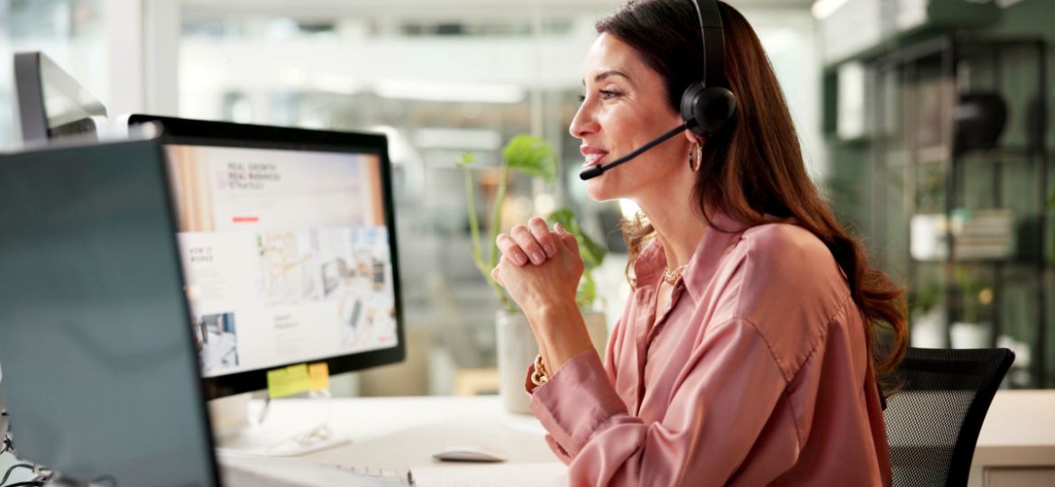 woman with headset looking at two computers